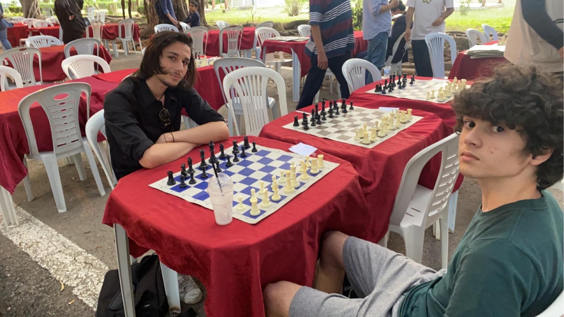 Deux joueurs assis devant un échiquier sur une table recouverte d’une nappe rouge.