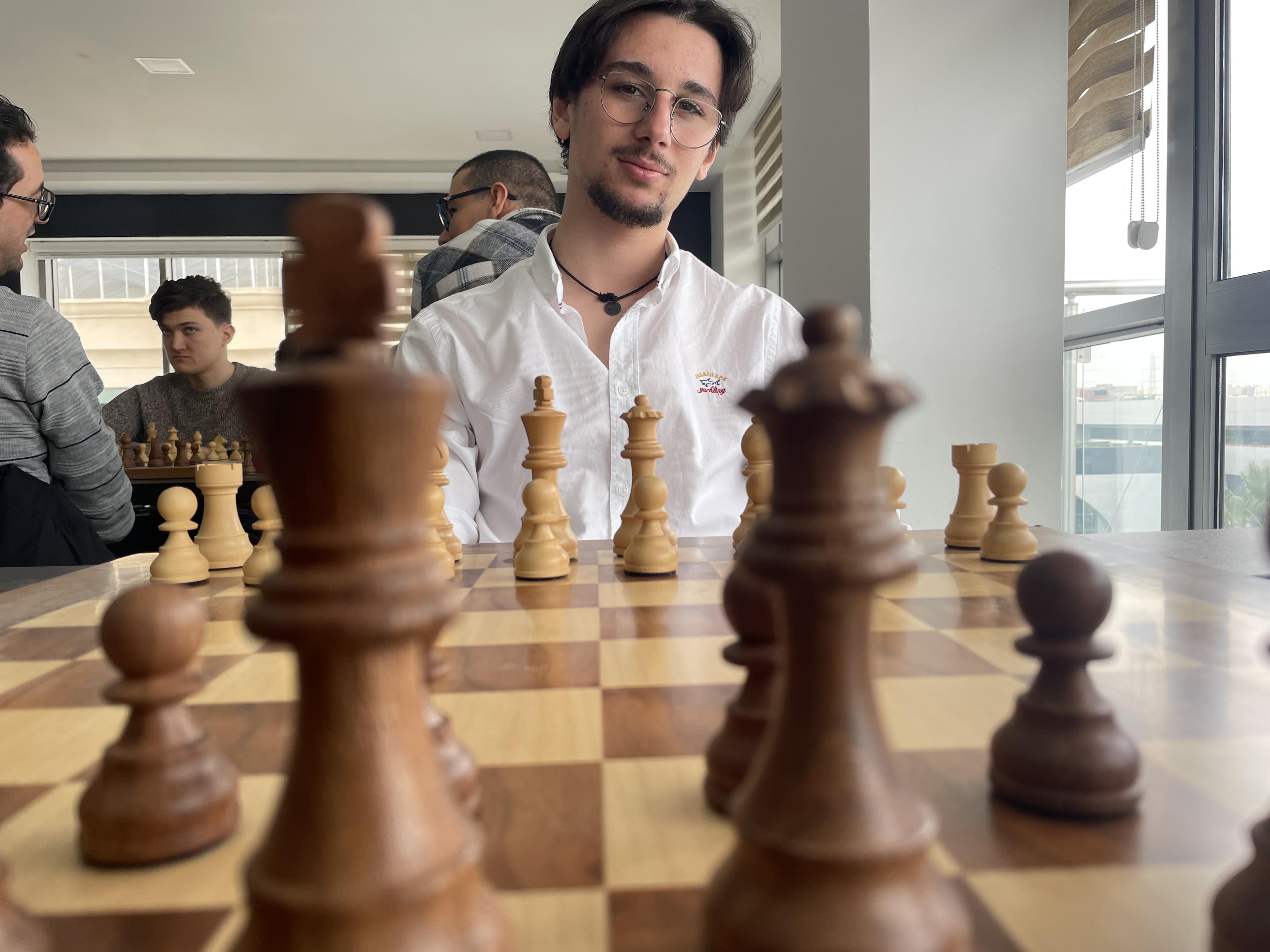 Un échiquier au premier plan et un joueur assis derrière.