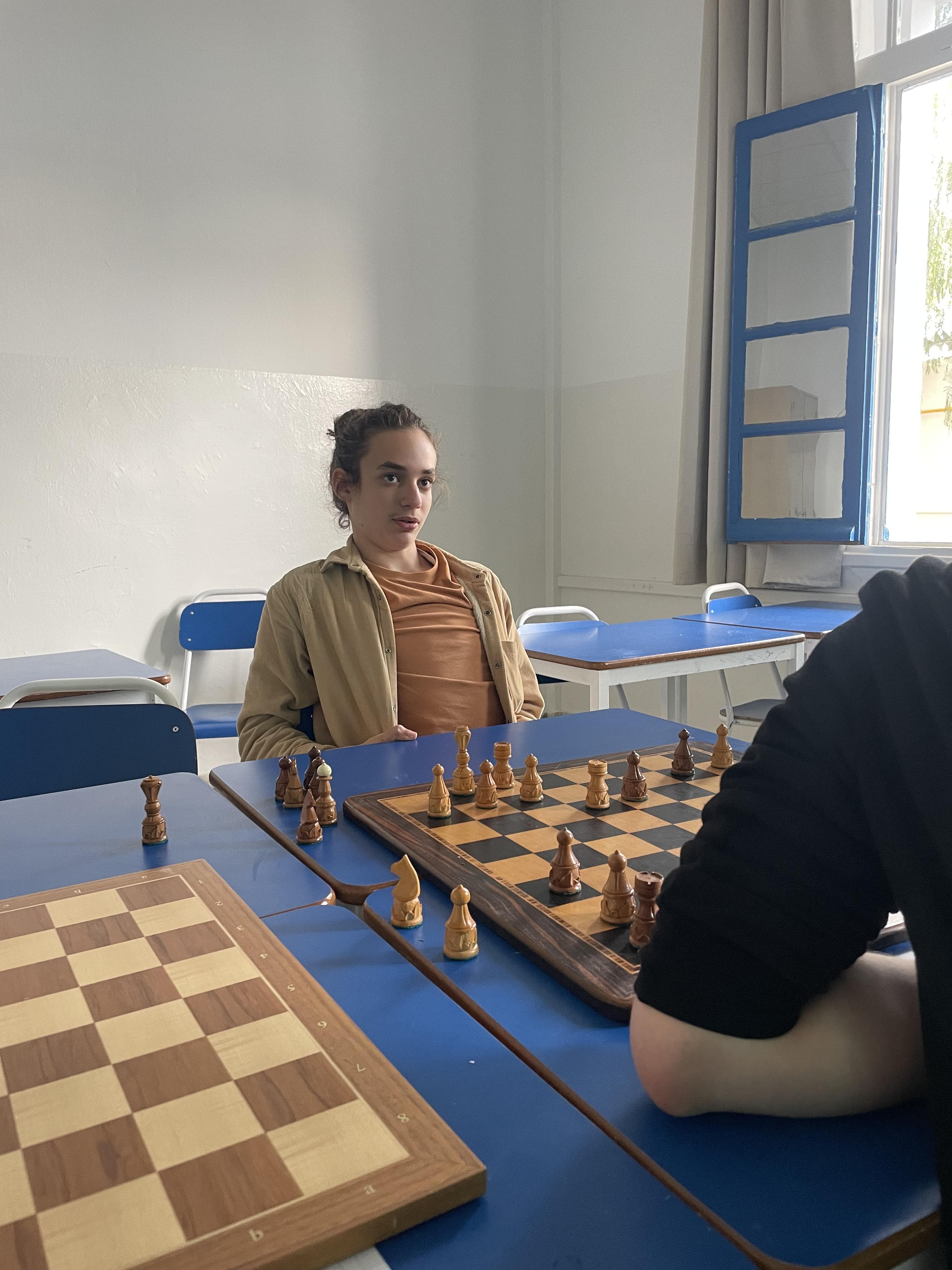 Deux personnes assises face à un échiquier dans une salle de classe.