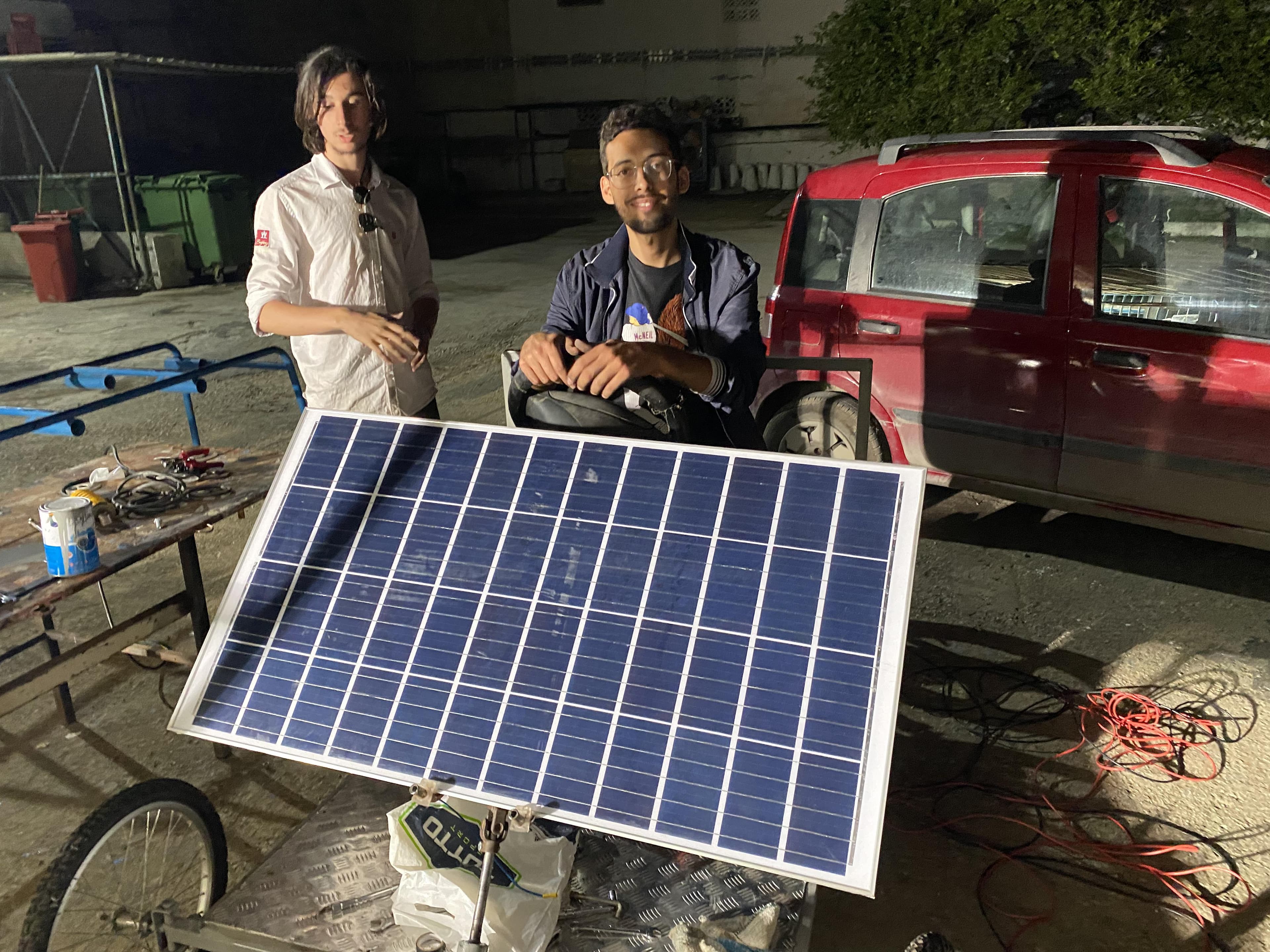Two people beside a vehicle prototype with a solar panel mounted at the front