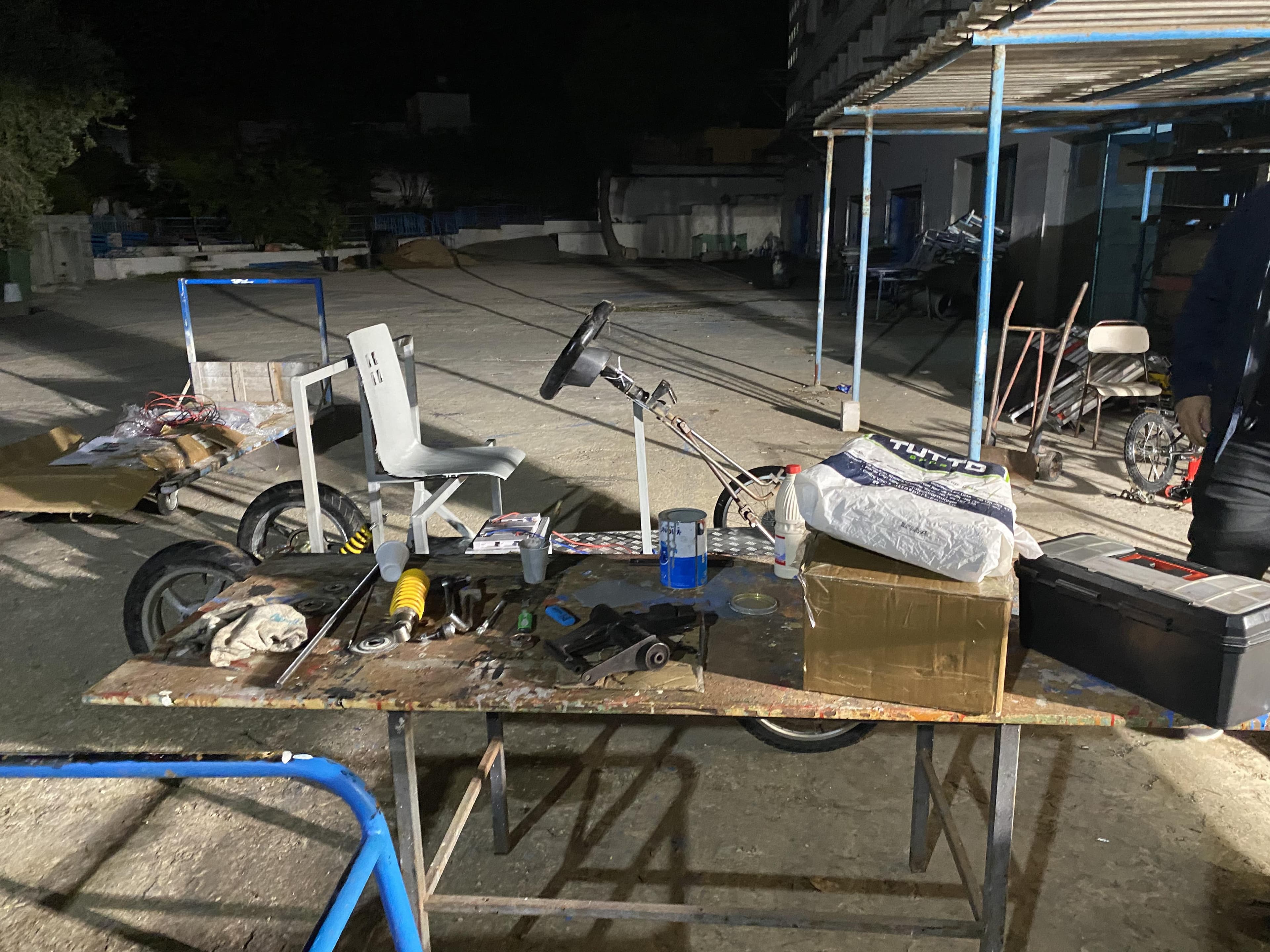 Vehicle chassis, seat and steering wheel surrounded by tools in a workshop at night